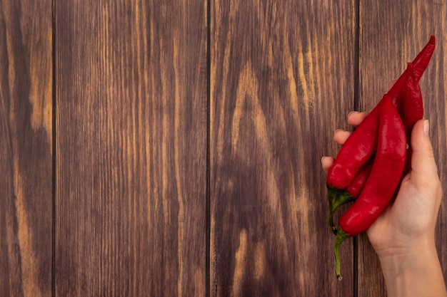 Vista superior de la mano femenina sosteniendo pimientos rojos frescos en una pared de madera con espacio de copia