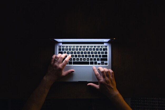 Vista superior de la mano de un hombre usando una computadora portátil a última hora de la noche