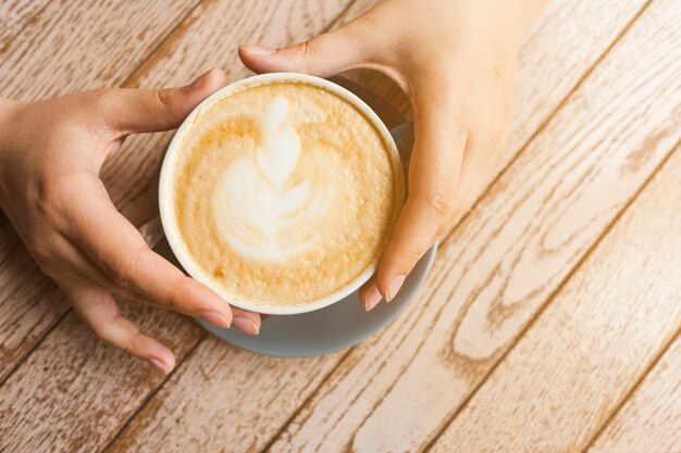 Vista superior de la mano humana que sostiene la taza de café del latte sobre superficie de madera