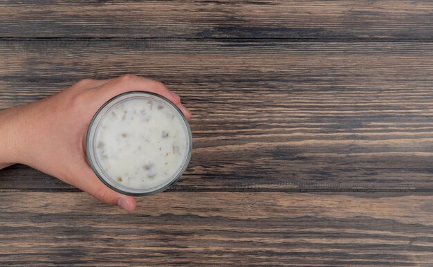 Vista superior de la mano masculina que sostiene un vaso de sopa de yogur sobre fondo de madera con espacio de copia