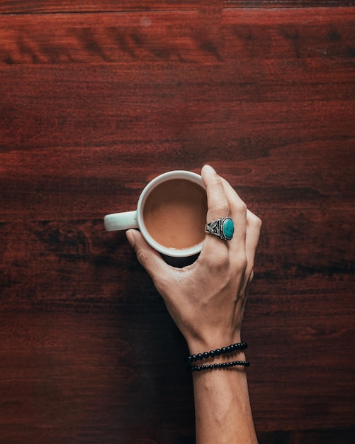 Foto gratuita vista superior de la mano de una mujer sosteniendo una taza blanca llena de café en una superficie de madera