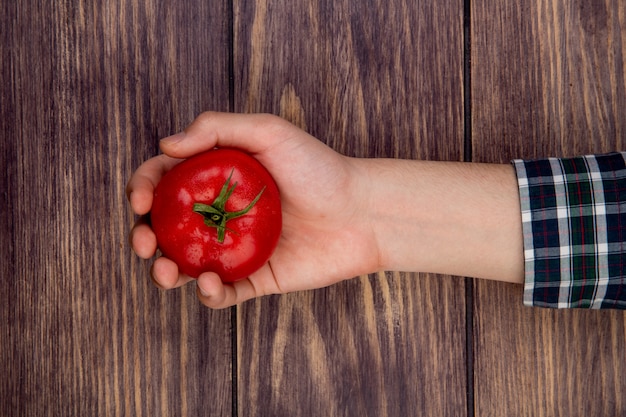 Vista superior de la mano de mujer con tomate en superficie de madera