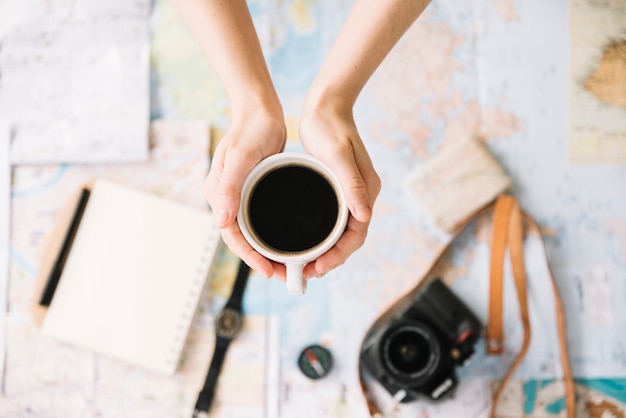 Vista superior de la mano de una persona que sostiene una taza de café sobre el mapa de un mundo borroso