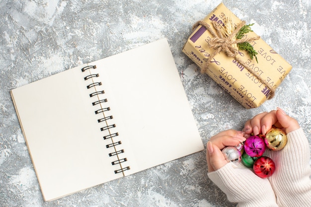 Vista superior de la mano que sostiene los accesorios de decoración de año nuevo, cuaderno abierto y regalo en la superficie del hielo