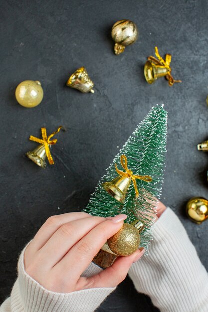 Vista superior de la mano que sostiene un árbol de Navidad y accesorios de decoración en la mesa oscura