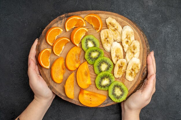 Vista superior de la mano que sostiene una fruta fresca orgánica natural en una tabla de cortar sobre una superficie oscura