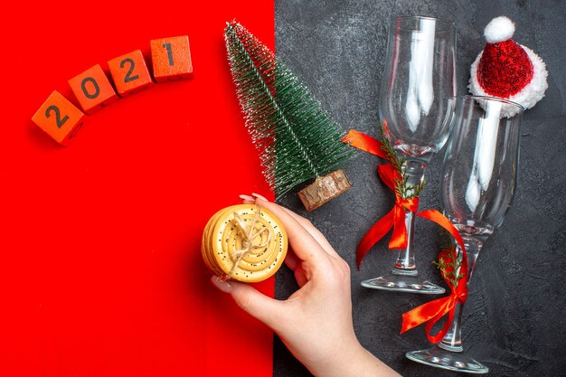 Vista superior de la mano que sostiene las galletas apiladas números de árbol de navidad sombrero de santa claus sobre fondo rojo y negro