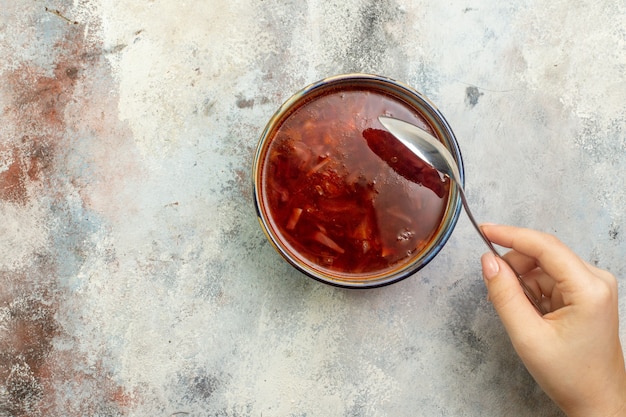 Vista superior de la mano sosteniendo una cuchara en una olla azul con deliciosa sopa de borscht sobre un fondo colorido