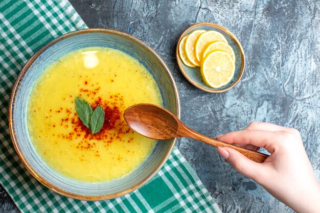 Vista superior de la mano sosteniendo una cuchara y una olla azul con sabrosa sopa servida con menta y pimienta