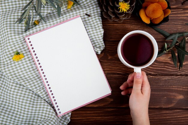 Vista superior de una mano sosteniendo una taza de té con cuaderno de bocetos en madera