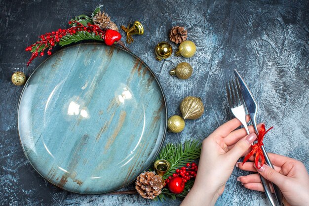 Vista superior de la mano sujetando cubiertos con cinta roja y plato azul vacío sobre fondo oscuro