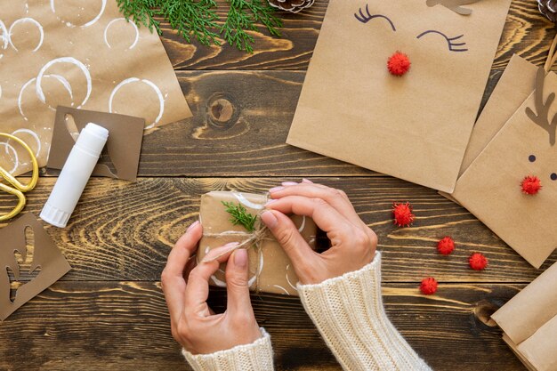 Vista superior de las manos atando el regalo de Navidad con una cuerda y una planta