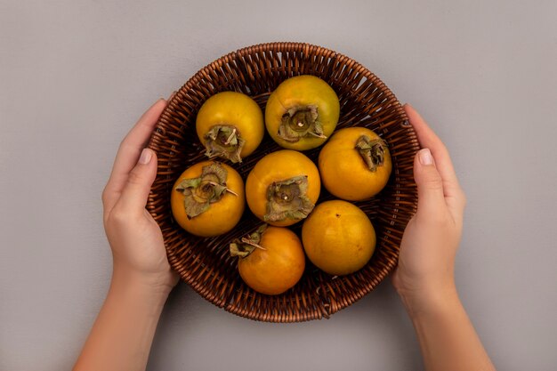 Vista superior de manos femeninas sosteniendo un balde de frutas de caqui