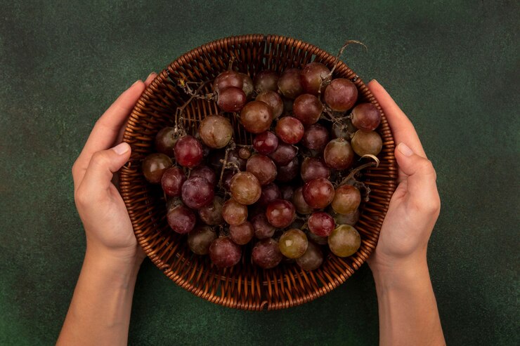 Foto gratuito vista superior de manos femeninas sosteniendo un balde de uvas frescas y saludables sobre una superficie verde
