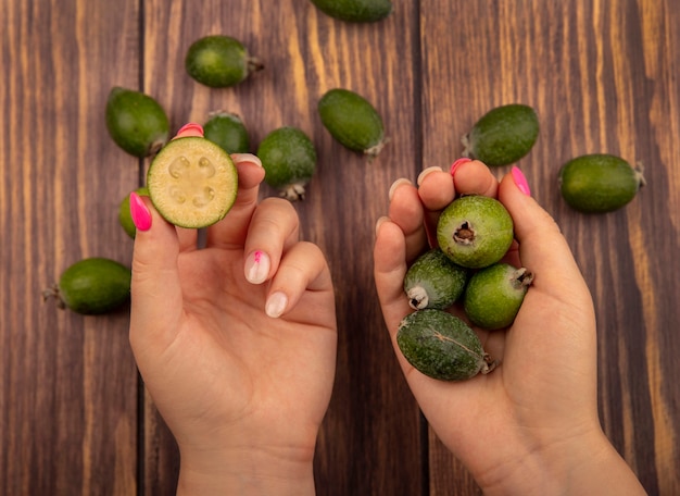 Vista superior de manos femeninas sosteniendo feijoas enteras y medias con feijoas aislado sobre un fondo de madera