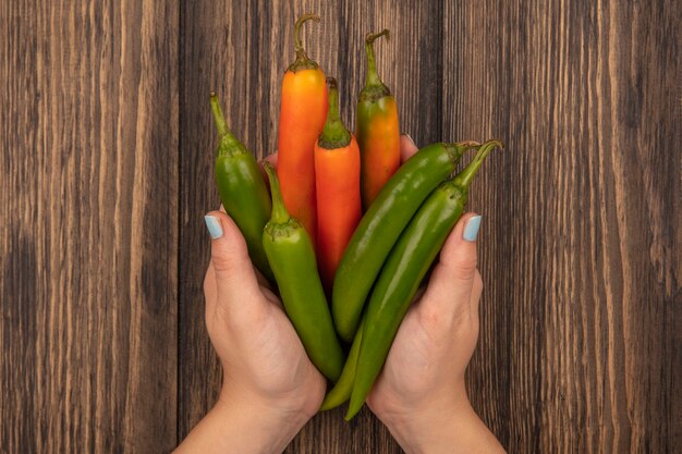 Vista superior de manos femeninas sosteniendo pimientos aromáticos frescos sobre una superficie de madera