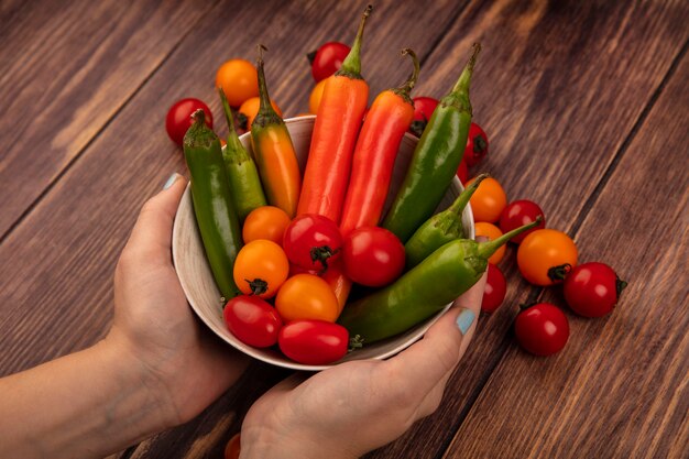 Vista superior de manos femeninas sosteniendo un plato de pimientos y tomates frescos en una pared de madera