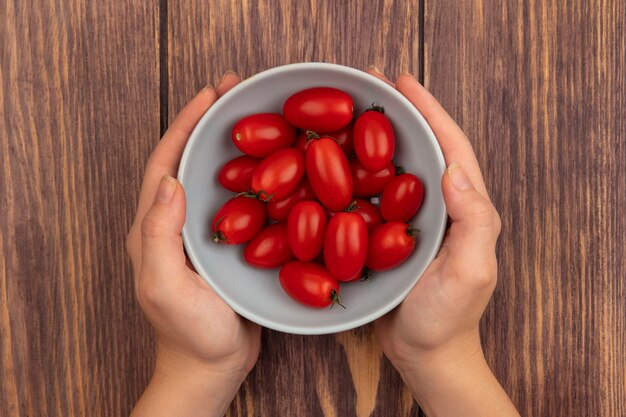 Vista superior de manos femeninas sosteniendo un plato de tomates frescos sobre una superficie de madera