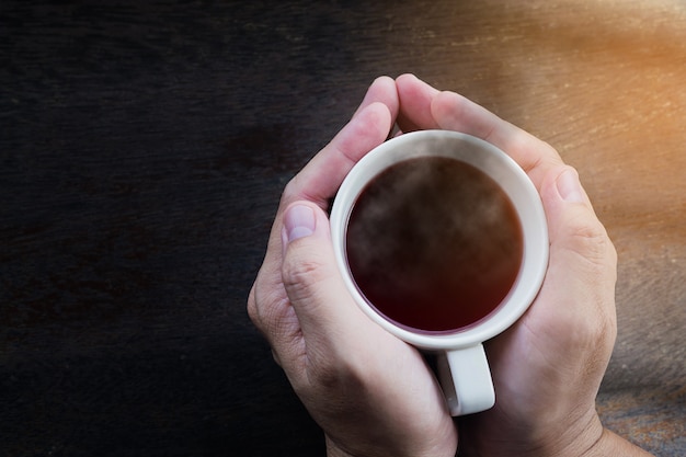 Vista superior de las manos del hombre que sostienen la taza de café caliente