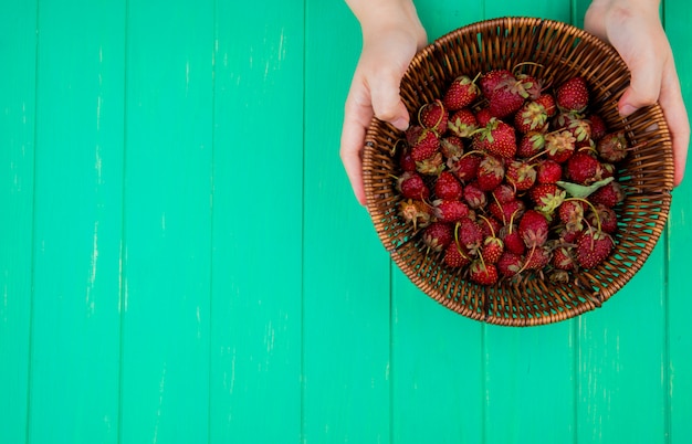 Vista superior de manos de mujer sosteniendo la cesta con fresas en el lado derecho y mesa verde