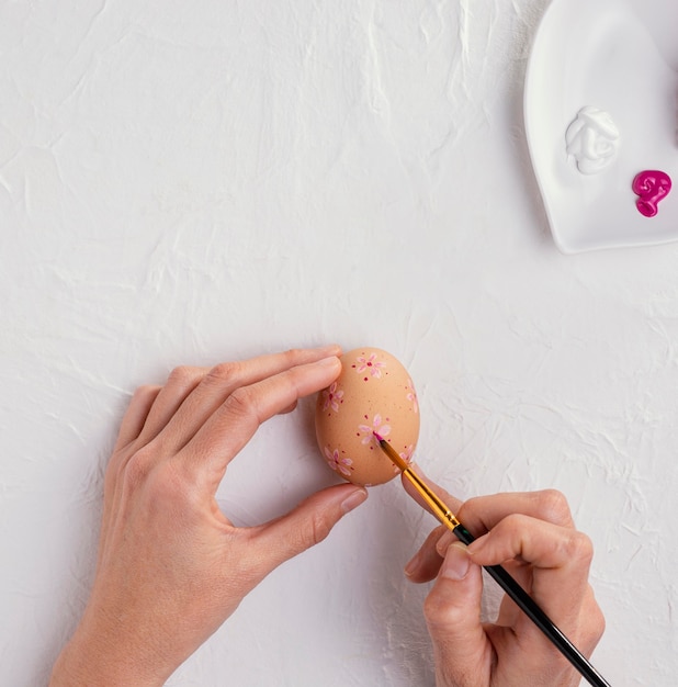 Vista superior de manos con pincel pintando huevos de Pascua