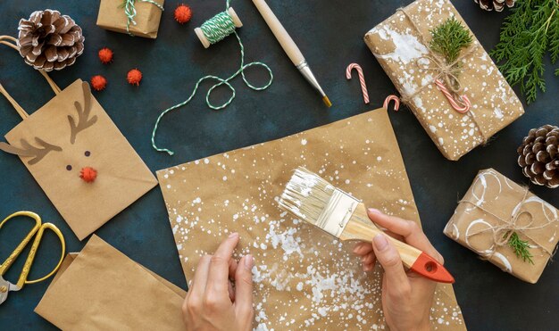 Vista superior de las manos con pincel sobre papel de regalo navideño