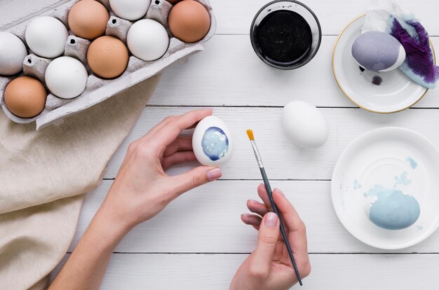 Vista superior de manos pintando huevo para pascua con cartón y tinte