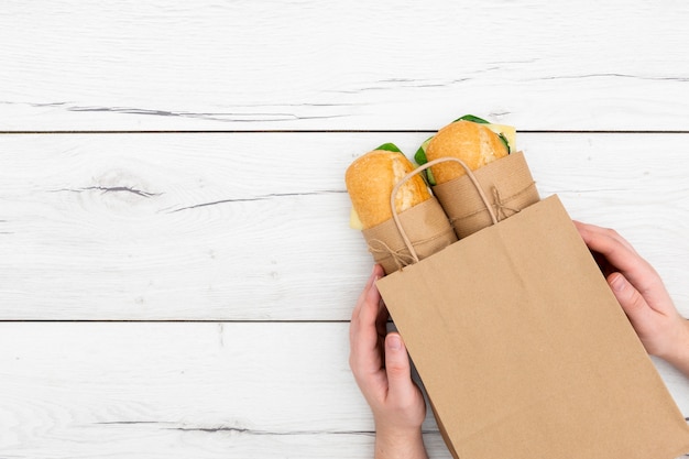 Vista superior de manos sosteniendo sándwiches en bolsa de papel