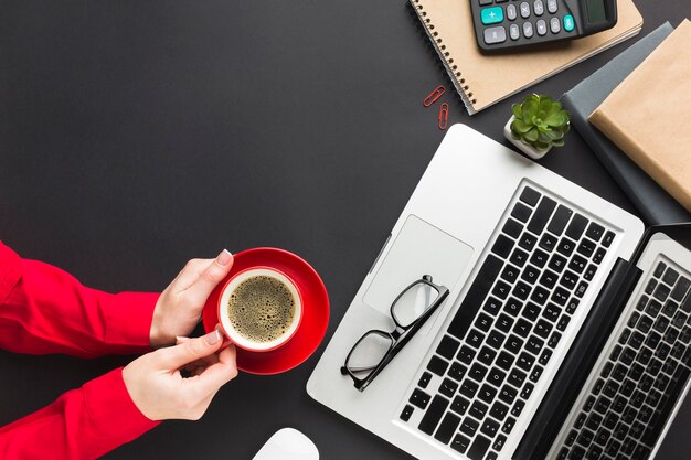 Vista superior de manos sosteniendo la taza de café en el escritorio