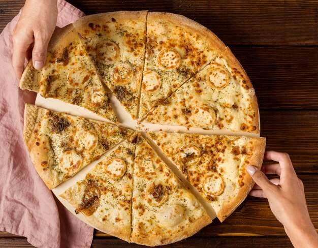 Vista superior de las manos tomando porciones de pizza con queso
