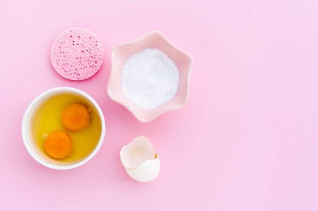 Vista superior de mantequilla corporal y huevos sobre fondo rosa