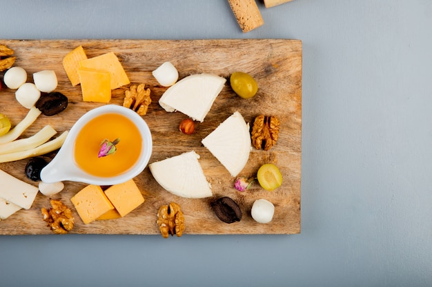 Vista superior de mantequilla derretida con diferentes tipos de queso uva nueces de oliva en la tabla de cortar en blanco con espacio de copia