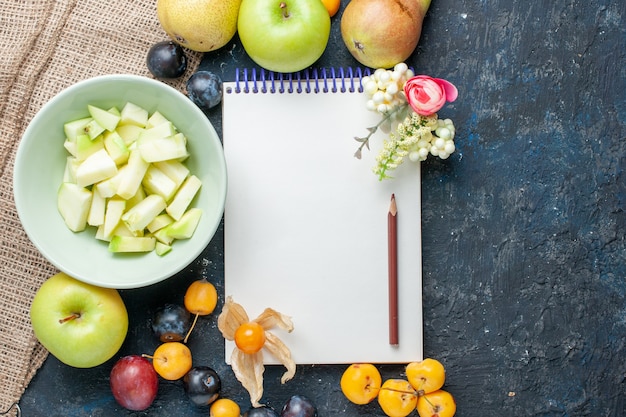 Vista superior de manzana verde en rodajas junto con diferentes frutas frescas y el bloc de notas en el fondo azul oscuro galleta de fruta dulce dulce