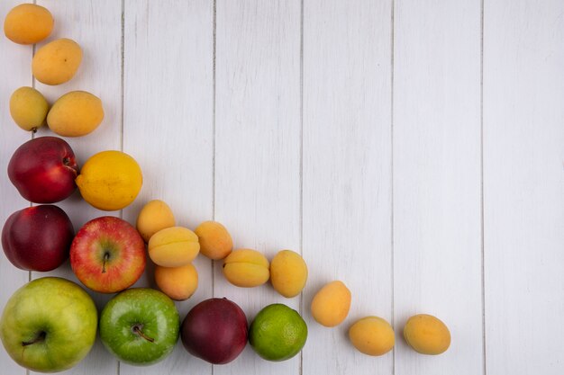 Vista superior de manzanas de colores con albaricoques y melocotones sobre una superficie blanca