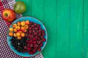 Foto gratuita vista superior de manzanas de colores con frambuesas, cerezas blancas y grosellas negras en un plato sobre una superficie verde