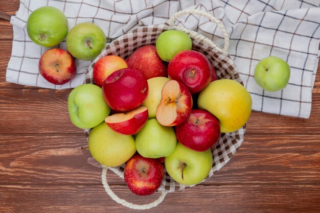 Vista superior de manzanas cortadas y enteras en la cesta y en tela escocesa sobre fondo de madera