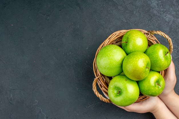 Vista superior de manzanas frescas en canasta de mimbre en mano femenina en el espacio libre de la superficie oscura