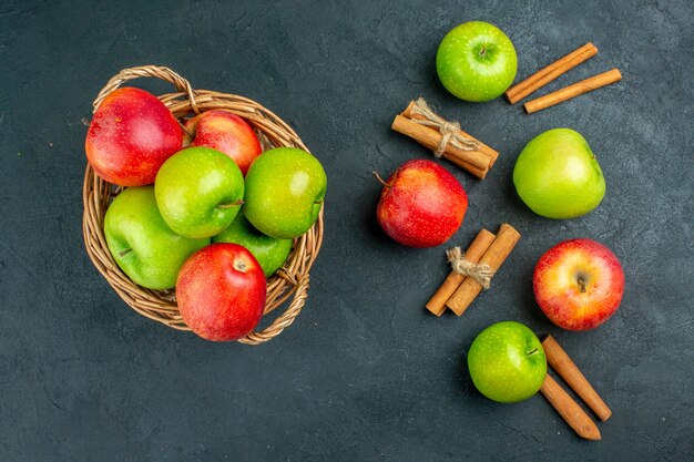 Vista superior de manzanas frescas en canasta de mimbre palitos de canela sobre superficie oscura