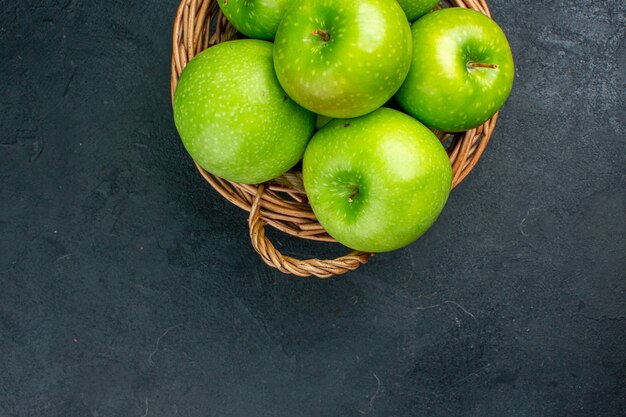 Vista superior de manzanas frescas en canasta de mimbre sobre superficie oscura