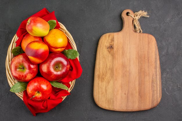 Vista superior de manzanas frescas con melocotones dentro de la canasta en la mesa oscura árbol de fruta fresca madura