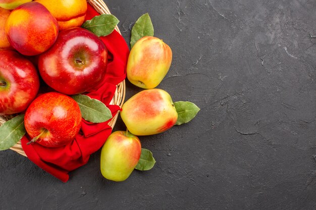 Vista superior de manzanas frescas con melocotones dentro de la canasta en la mesa oscura árbol frutal maduro fresco