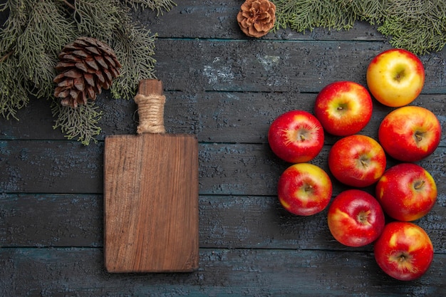 Vista superior de las manzanas y junta nueve manzanas y una tabla de cortar debajo de las ramas de los árboles con conos