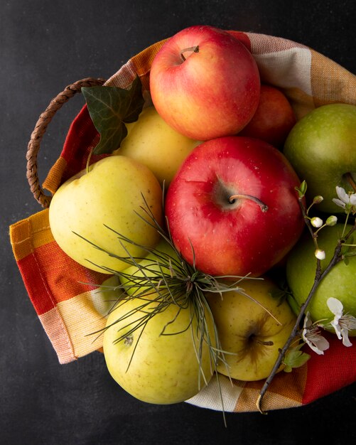 Vista superior de manzanas multicolores en una cesta con una ramita de flores
