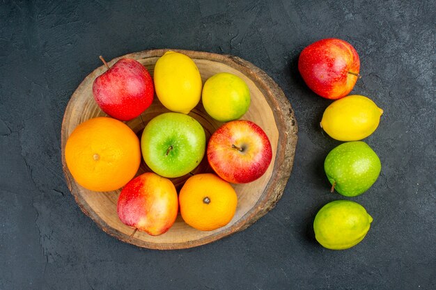 Vista superior de las manzanas, las naranjas de limón en la tabla de cortar rústica en la superficie oscura.