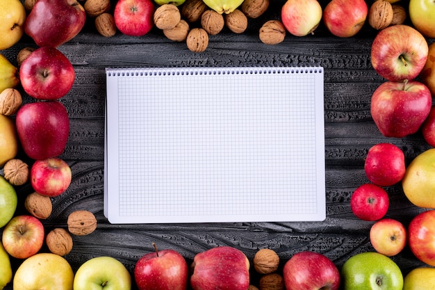 Vista superior de manzanas y peras con nueces y nueces con espacio de copia en el cuaderno en madera gris