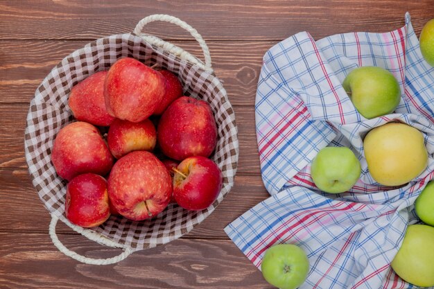 Vista superior de manzanas rojas en canasta con verdes en tela escocesa sobre fondo de madera