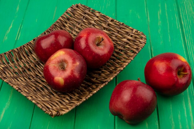 Vista superior de manzanas rojas frescas en una bandeja de mimbre en una pared de madera verde