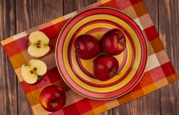 Vista superior de manzanas rojas frescas en un plato sobre una tela marcada con manzanas cortadas por la mitad aislado en una pared de madera