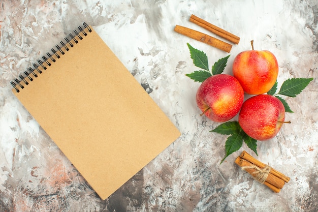Vista superior de manzanas rojas naturales frescas y limas canela y cuaderno de espiral sobre fondo de colores mezclados
