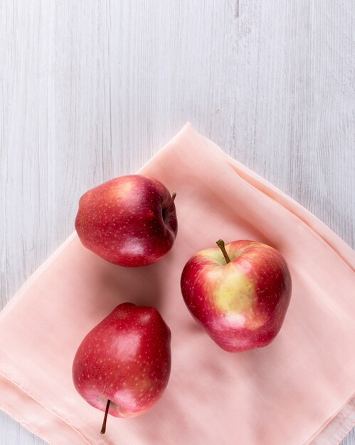 Vista superior de manzanas rojas con tela rosa en blanco vertical de madera
